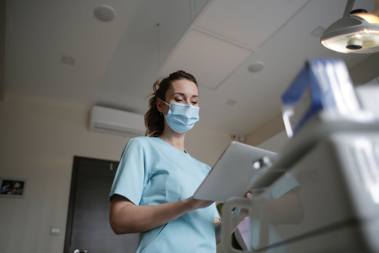 about-img Female healthcare worker wearing a mask and holding a clipboard in a clinical environment.