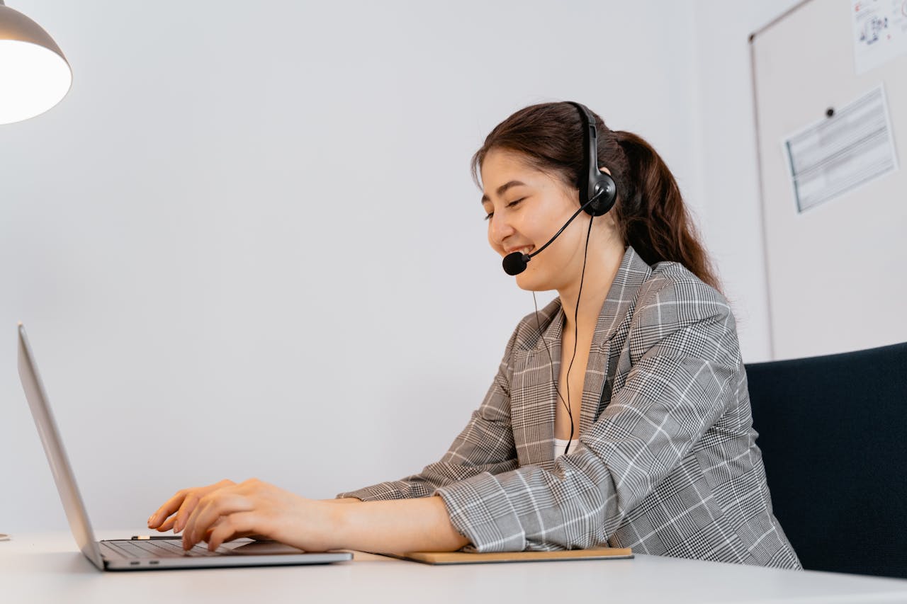 services-img Woman in a plaid blazer working at a laptop with a headset in an office setting.